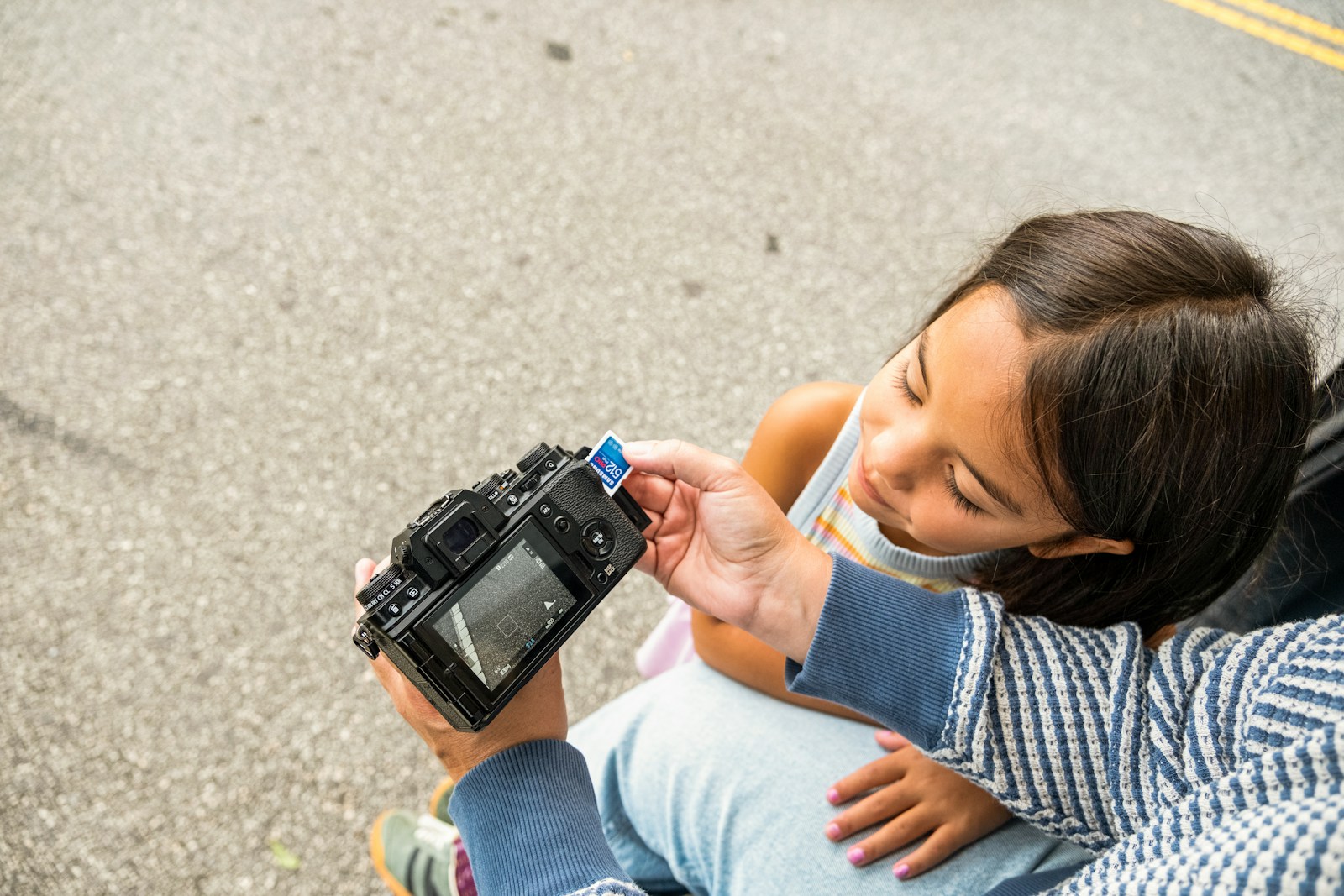 A girl looks at a camera held by an adult.